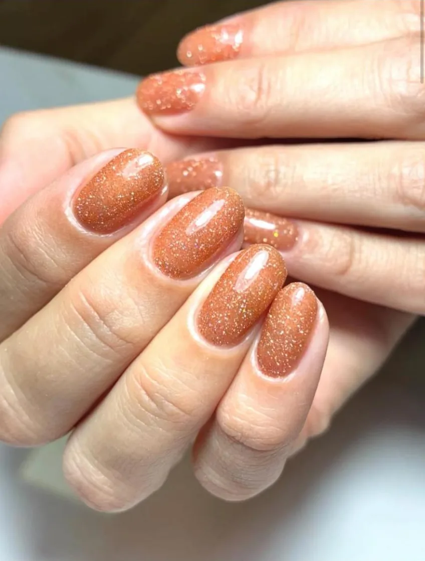 Unhas curtas arredondadas em cobre com glitter